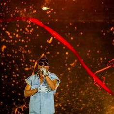 a man standing in front of a stage holding a microphone to his mouth while wearing sunglasses