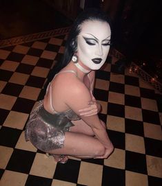 a woman with white face paint sitting on a checkered floor