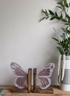 two butterflies are sitting next to each other on a wooden shelf near a vase with flowers