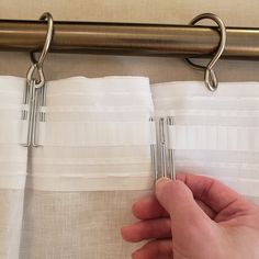 a hand is pulling the curtain tabs off of a pair of metal hooks on a white curtain