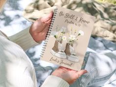 a woman holding up a book with flowers on the front and bottom cover, which reads be still & know