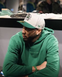 a man with a beard wearing a green hoodie and white cap sitting in front of a counter