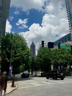 a city street with tall buildings and cars driving down it's road under a cloudy blue sky