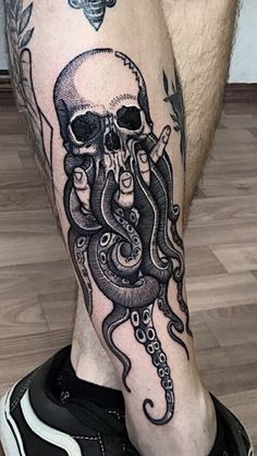 an octopus and skull tattoo on the legs of a man with black ink, sitting on a wooden floor