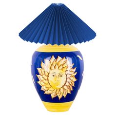 a blue and yellow vase with a sun design on the side, under a paper fan