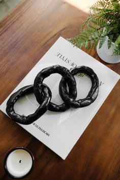 two black rings sitting on top of a wooden table next to a candle and plant