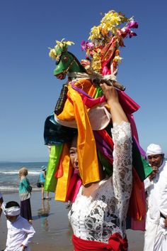 a woman is standing on the beach with her head covered in colorful cloths and flowers