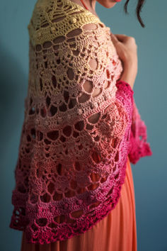 a woman in an orange dress is wearing a pink and yellow crocheted shawl