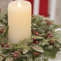 a candle is lit in front of a wreath with holly and pine cones on it