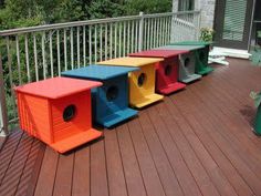 four different colored bird houses on a deck