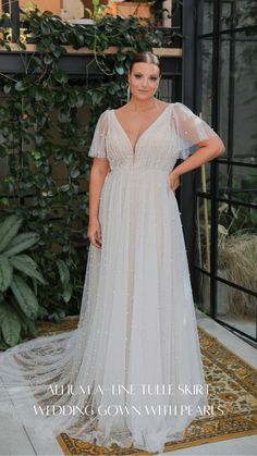 a woman standing in front of a plant wearing a wedding gown with sheer sleeves and beading