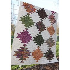 a quilt hanging on the side of a fence in front of some grass and trees