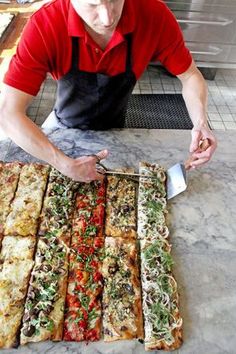 a man in an apron is cutting pizzas on a table