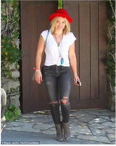 a woman with a red hat is standing in front of a brown door wearing black jeans and boots