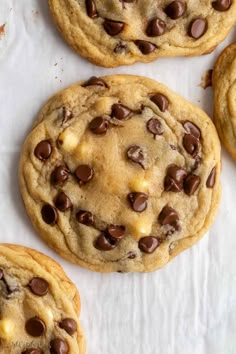 four chocolate chip cookies sitting on top of a white paper towel next to each other