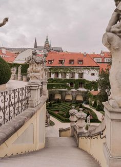 an ornate balcony with statues and hedges in the foreground, surrounded by red roofed buildings