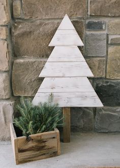 a small wooden christmas tree sitting next to a potted plant