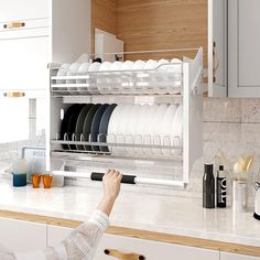 a woman is looking at dishes in the dish rack on the kitchen counter, while she's holding her hand up