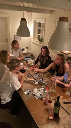 a group of people sitting around a wooden table with wine bottles and cards on it