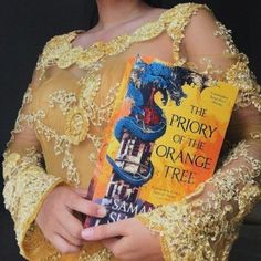 a woman holding a book in her hands and wearing a yellow dress with an elaborate dragon on it