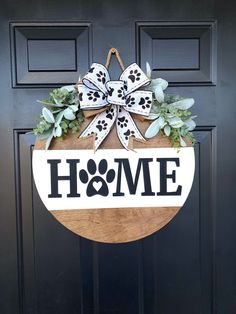 a dog door hanger that says home with a bow and paw prints on it