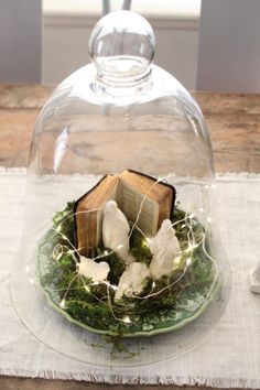 an open book under a glass dome on top of a green plate with white flowers