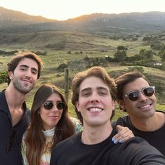 three people taking a selfie in front of a mountain range with the sun setting behind them