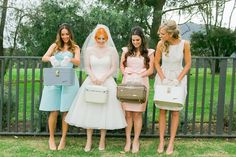 four bridesmaids pose for a photo in front of a fence with their purses