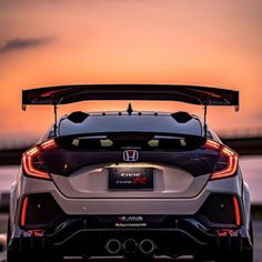 the back end of a white car with its hood open at sunset in front of a body of water