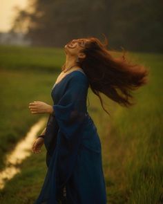 a woman with her hair blowing in the wind on a path through a grassy field