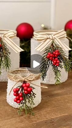 three mason jars decorated with holly and red berries are sitting on a wooden table in front of christmas decorations