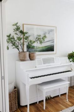 a white piano sitting in the corner of a living room next to a potted plant