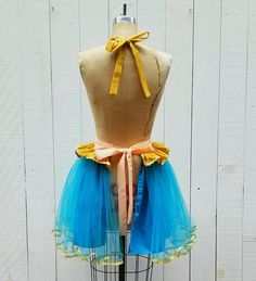 a mannequin wearing a blue and yellow tutu skirt on top of a wooden stand