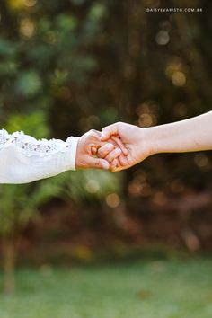 two people holding hands in front of some trees