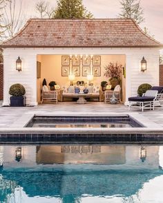 an outdoor living area next to a swimming pool with chairs and tables around it, in front of a white brick house