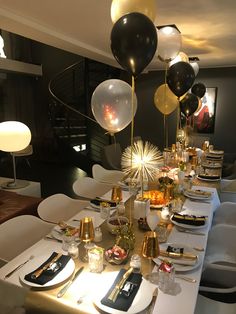 a long table with black and white balloons on it, gold rimmed plates and silverware