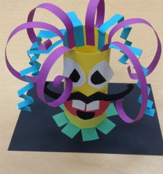 an origami mask with purple ribbon around it's neck and mouth, on top of a black card board