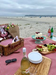 a picnic table set up on the beach with wine, fruit and cake for two