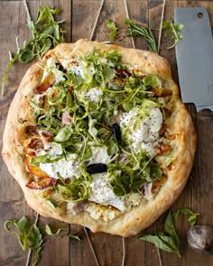 a pizza sitting on top of a wooden table next to a knife and some greens