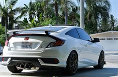 the rear end of a white honda civic hatchback parked in front of palm trees