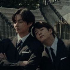 two young men sitting next to each other in suits and ties with their arms crossed