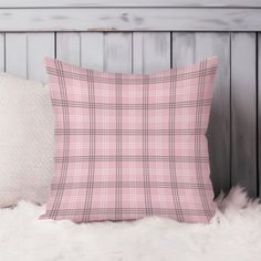 a pink plaid pillow sitting on top of a white fur rug