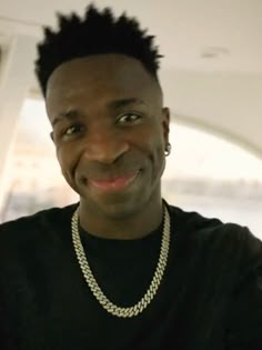 a man with a black shirt is smiling at the camera while wearing a chain around his neck