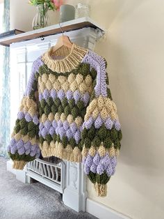 a knitted sweater hanging on the wall next to a vase with flowers in it