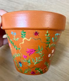 a hand holding an orange flower pot with flowers painted on it