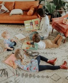 three children are sitting on the floor reading books and playing with their mother in the living room