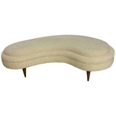 an oval shaped bench with wooden legs and a white upholstered cushion on it