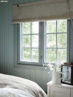 a bedroom with blue walls, white bedding and a window that has blinds on it