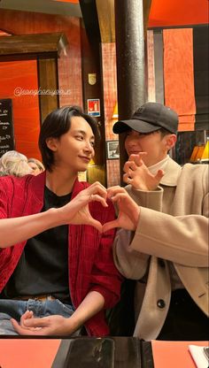 two people sitting at a table making a heart with their hands