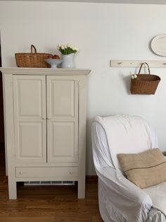 a white arm chair sitting next to a wooden cabinet and basket on top of it